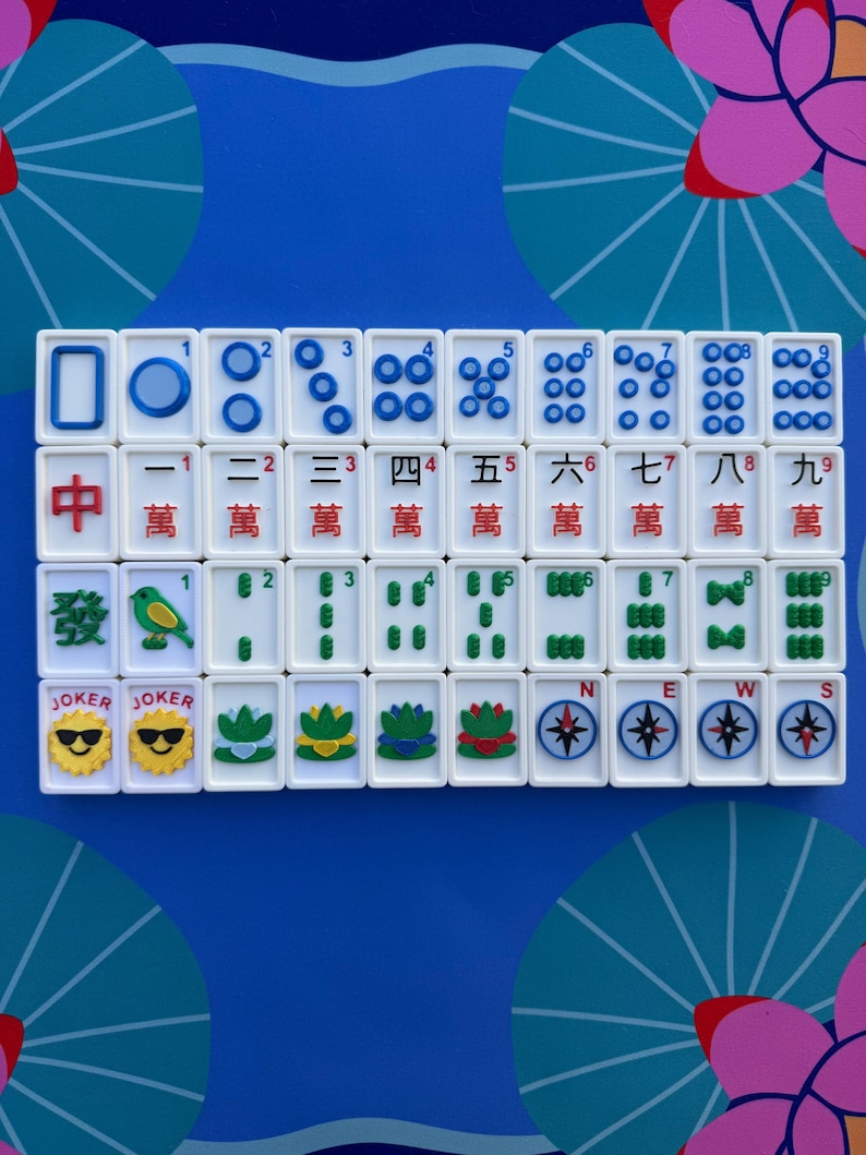 May include: A set of white Mahjong tiles with blue and red markings, arranged on a blue surface with floral designs. The tiles feature Chinese characters, numbers, and suit symbols, including Jokers and compass directions.