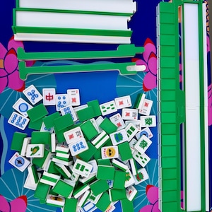 May include: A complete Mahjong set with green and white components, including tiles and racks, arranged on a blue surface with floral accents. The tiles feature various symbols and characters. The text "NO Jokers ALLOW IN news" is visible.