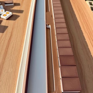 May include: A wooden board game set with a light brown and white frame, a gray playing surface, and brown rectangular game pieces. The set is on a wooden table.