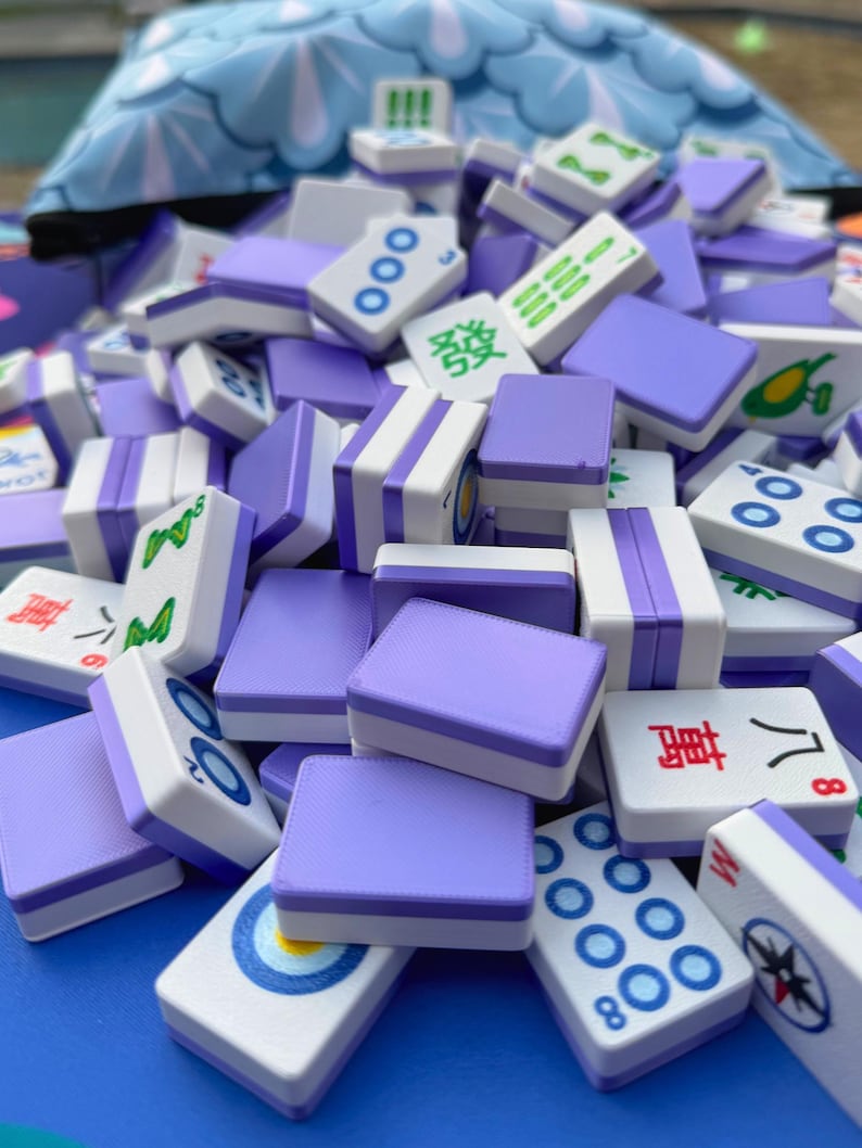 May include: A pile of Mahjong tiles in shades of purple and white. The tiles feature various symbols and characters, including circles, lines, and Chinese characters. The tiles are stacked, creating a visually appealing arrangement.