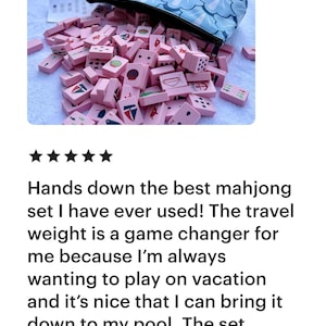 May include: A pink mahjong set with a blue patterned carrying case. The tiles are pink with various symbols and numbers. The set is spilling out of the case. The text in the image says: "Hands down the best mahjong set I have ever used!"