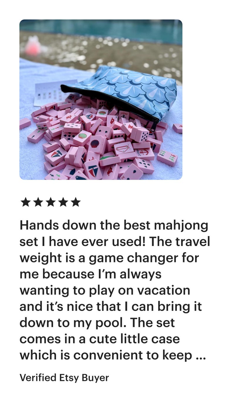 May include: A pink mahjong set with a blue patterned carrying case. The tiles are pink with various symbols and numbers. The set is spilling out of the case. The text in the image says: "Hands down the best mahjong set I have ever used!"