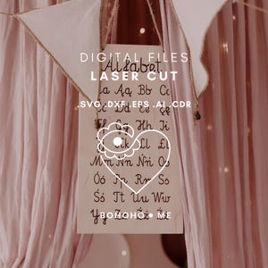 May include: A wooden sign featuring the alphabet in a handwritten style, with the words "DIGITAL FILES" and "LASER CUT" at the top. The sign is suspended by a gold chain, set against a pink backdrop.
