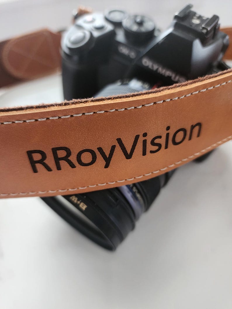 May include: A brown leather camera strap with the text "RRoyVision" embossed in black.