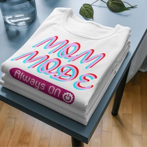 May include: A white t-shirt with the text "MOM MODE" in pink, blue, and red letters. The text "ALWAYS ON" is in a purple rectangle with a power button icon.