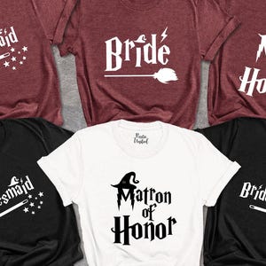 May include: A collection of t-shirts in burgundy, black, and white. The shirts feature white text and graphics, including the words "Bridesmaid," "Bride," and "Maid of Honor," with witch-themed designs. The shirts are likely for a bridal party.