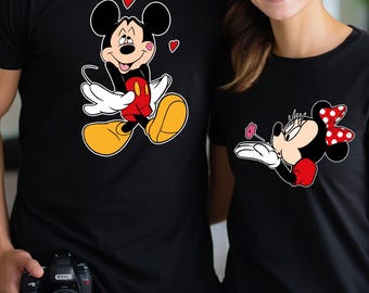 May include: Matching black t-shirts featuring Mickey and Minnie Mouse. The Mickey shirt has a cartoon image of Mickey with hearts, and the Minnie shirt has Minnie with a red bow. Both shirts are short-sleeved.