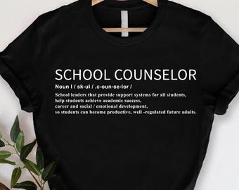 May include: Black t-shirt with the text "SCHOOL COUNSELOR" in white. The definition of a school counselor is printed below the title. The shirt is hanging on a wooden hanger.