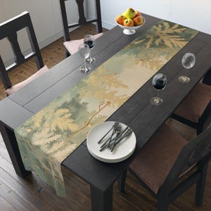 May include: A dining table set for a meal, featuring a decorative table runner with a forest design in shades of green and gold. The table is set with plates, silverware, wine glasses, and a bowl of fruit. The table and chairs are dark wood.