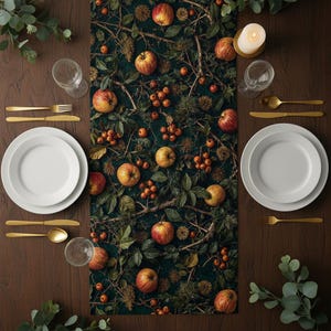 May include: A table setting with a dark green runner featuring a pattern of apples, berries, and foliage. White plates, gold cutlery, and clear glasses are arranged on a dark wooden table. A lit candle adds a warm glow.