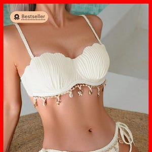 May include: White bikini top and bottom with a seashell design and gold accents. The top has a scalloped edge and the bottom has a tie side.