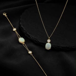 May include: A gold-toned necklace and bracelet set featuring oval-shaped opalescent stones and small, clear, round-cut accent stones. The necklace has a delicate chain with a pendant, while the bracelet features a matching chain and stone design.