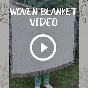 Puede incluir: Una manta tejida rectangular con un centro beige claro y bordes con flecos multicolores. El texto WOVEN BLANKET VIDEO está impreso en blanco en la parte superior central, y un icono de botón de reproducción blanco está centrado en la manta.