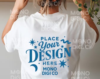 Op de afbeelding: Wit t-shirt met een blauw ontwerp op de achterkant met de tekst "Place Your Design Here" met ster- en halve maan-afbeeldingen. Het shirt wordt gedragen door een persoon met een perzikkleurige scrunchie in het haar.