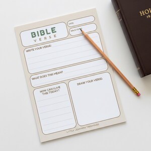 May include: A beige Bible Verse notepad with a pencil and a closed brown book. The notepad has sections for writing a Bible verse, its meaning, and how to apply it. The notepad also has a section to draw a verse. The text "BIBLE VERSE" is at the top.