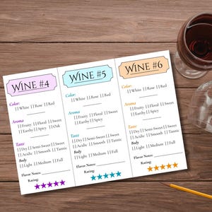 May include: A wine tasting setup with three wine information cards, a bottle of red wine, and two wine glasses. The cards list color, aroma, taste, and body. A pencil rests on the wooden surface.