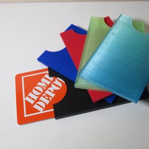 May include: A stack of five plastic card holders in various colours, including blue, red, green, and light blue. The top card holder is light blue and has a Home Depot gift card underneath it.