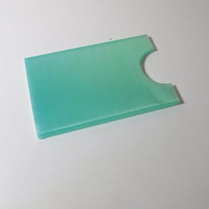 May include: A light green plastic card holder with a cutout for a card. The holder is smooth and has a slight sheen.