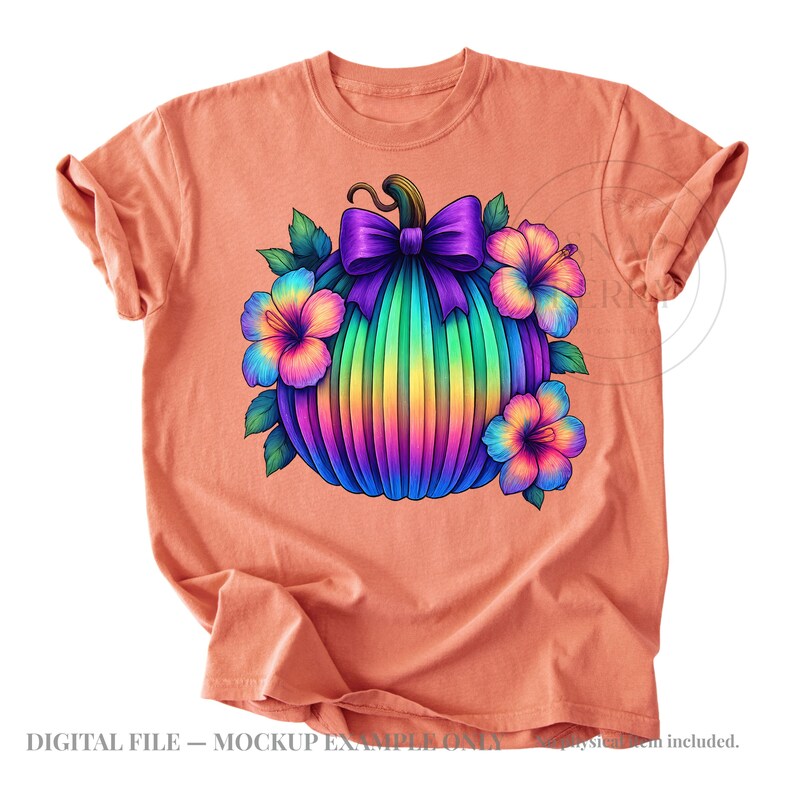 May include: A peach-colored t-shirt featuring a central graphic of a pumpkin with a rainbow gradient, topped with a large purple bow and surrounded by colorful hibiscus flowers with green leaves. The design is vibrant and multi-colored.