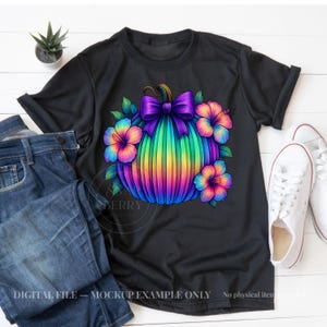 May include: A black short-sleeved t-shirt featuring a graphic of a rainbow-colored pumpkin with a purple bow on top, surrounded by colorful hibiscus flowers. The shirt is displayed alongside blue denim jeans and white sneakers.