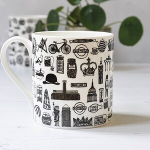 May include: White ceramic mug featuring a black and white illustration of London landmarks, including Big Ben, the London Eye, and a double-decker bus. The mug also features the text "Fish & Chips" and "Oxford Street".