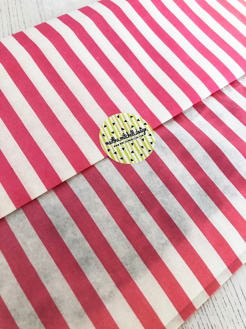 May include: A pink and white striped paper bag with a round sticker that says "marla mitchell design" and "www.marlamitchelldesign.com".