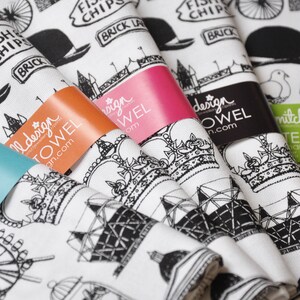 Może przedstawiać: Zestaw pięciu ręcznik&oacute;w kuchennych z czarno-białymi ilustracjami londyńskich zabytk&oacute;w, w tym London Eye, Big Ben i Tower Bridge. Ręczniki są białe z czarnym tekstem, kt&oacute;ry brzmi "Fish Chips Brick Lane" i "Mitchell Design Tea Towels Handmade Cotton".