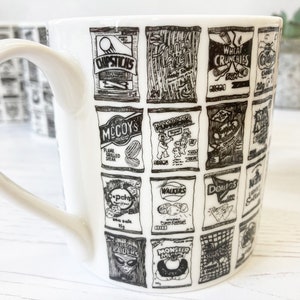 May include: White ceramic mug with a black and white design of various British snack food brands, including McCoy's, Walkers, and Wheat Crunchies.