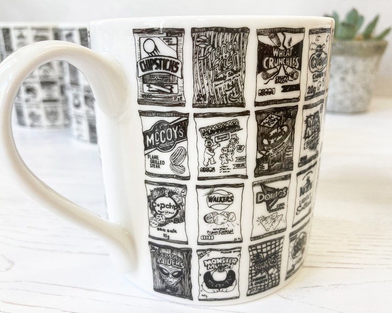 May include: White ceramic mug with a black and white design of various British snack food brands, including McCoy's, Walkers, and Wheat Crunchies.