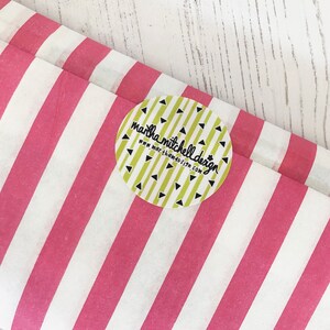 Może przedstawiać: Biały i r&oacute;żowy papier tiulowy w paski z okrągłą naklejką, na kt&oacute;rej widnieje napis "martha mitchell design" i "www.marthamitchelldesign.com" czarnym kolorem na ż&oacute;łtym tle z czarnymi tr&oacute;jkątami.