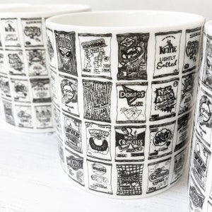 May include: A white ceramic mug with a black and white design of various snack food bags. The bags include brands like Monster Munch, McCoy's, Walkers, and Doritos.