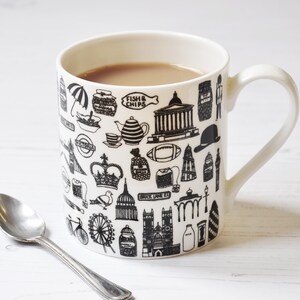 May include: A white ceramic mug with a black and white design featuring iconic London landmarks, including Big Ben, the London Eye, and a double-decker bus. The mug is filled with a brown liquid, likely tea or coffee.