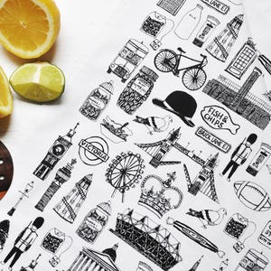 Może przedstawiać: Biały ręcznik do herbaty z czarno-białą ilustracją londyńskich zabytk&oacute;w i symboli. Projekt zawiera London Eye, Big Ben, autobus piętrowy, czerwoną budkę telefoniczną, koronę oraz napisy "VICTORIA", "FISH & CHIPS", "BRICK LANE E1" i "CARNABY STREET W1".