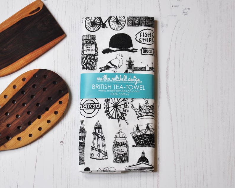 Może przedstawiać: Czarno-biały ręcznik do herbaty z motywem Londynu. Wz&oacute;r przedstawia ikoniczne zabytki, takie jak London Eye, Big Ben i piętrowy autobus. Tekst na ręczniku brzmi "FISH & CHIPS", "BRICK LANE", "VICTORIA" i "BRITISH TEA-TOWEL".