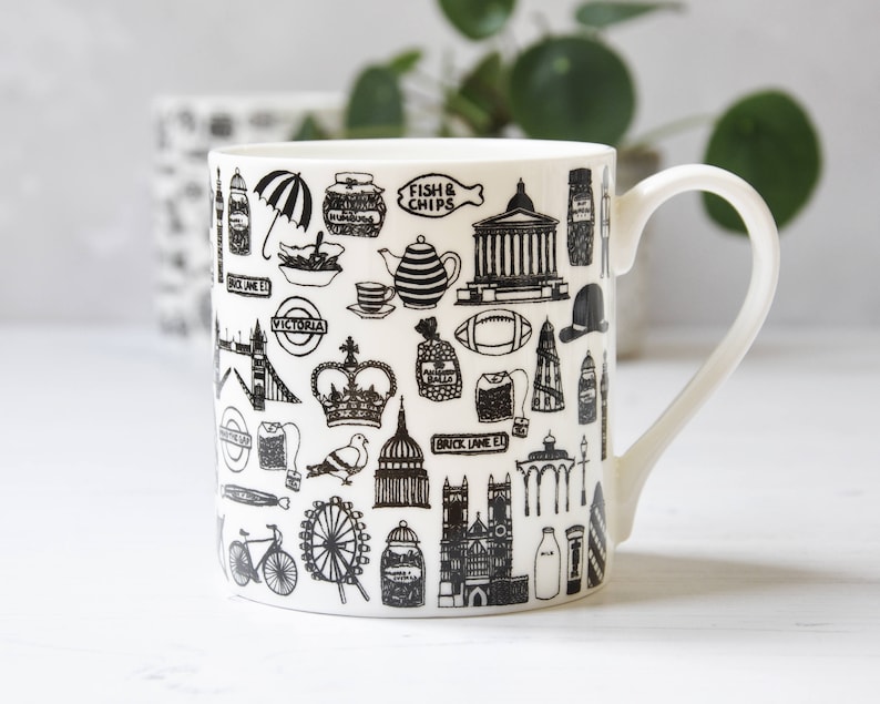 May include: White ceramic mug with a black and white design featuring iconic London landmarks, including Big Ben, the London Eye, and a double-decker bus. The text "Fish & Chips" and "Brick Lane E1" are also included in the design.
