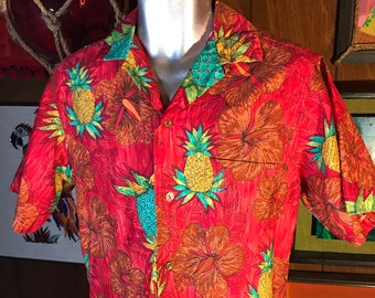 May include: A red short-sleeved button-down shirt with a tropical print featuring pineapples and hibiscus flowers in shades of green, yellow, orange, and brown.