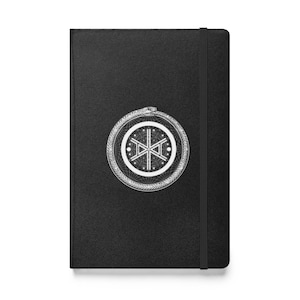 May include: Black journal with a white geometric design featuring a snake eating its tail. The design is circular and centered on the front cover. A black elastic band secures the journal.