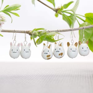 May include: A set of six ceramic animal earrings. Two white bunny earrings, two white cat earrings with brown spots, and two white cat earrings with brown stripes.