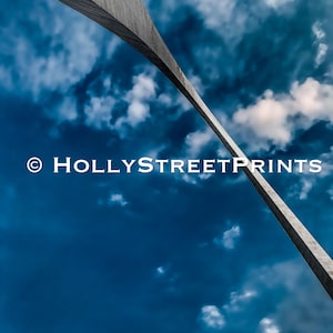 May include: A low angle view of the Gateway Arch in St. Louis, Missouri, with a blue sky and white clouds in the background. The arch is made of stainless steel and is a popular tourist destination.