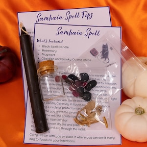 May include: A Samhain spell kit featuring a black candle, rosemary, mugwort, and obsidian and smoky quartz chips. The kit includes a small glass jar, a black candle, and instructions. Two white pumpkins and a red pumpkin are also in the image.