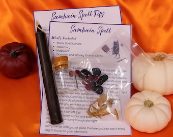 May include: A Samhain spell kit featuring a black taper candle, a small glass corked jar, a clear plastic bag containing dark stone chips and dried herbs, and two printed instruction cards, accompanied by one red and two white pumpkins.