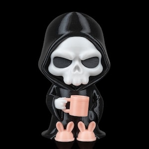 K&ouml;nnte beinhalten: 3D-gedruckte Figur des Sensenmanns in einer schwarzen Kapuzenrobe, die eine rosa Tasse h&auml;lt und rosa Hasenpantoffeln tr&auml;gt. Die Figur hat ein wei&szlig;es Totenkopfgesicht und ist vor schwarzem Hintergrund platziert.
