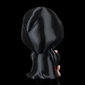 K&ouml;nnte beinhalten: Eine schwarze Figur einer Kapuzenfigur, m&ouml;glicherweise der Sensenmann, mit einem flie&szlig;enden Gewand. Die Figur h&auml;lt ein kleines, hellfarbiges Objekt. Die Figur ist vor einem schwarzen Hintergrund platziert.