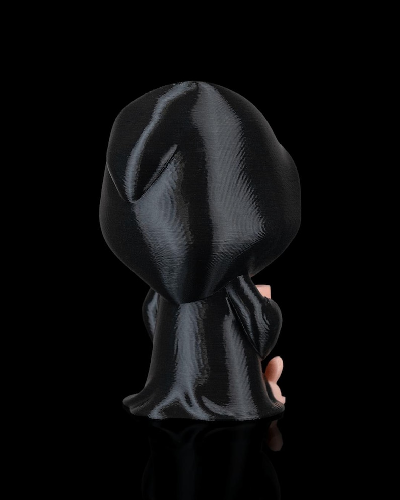 K&ouml;nnte beinhalten: Eine schwarze Figur einer Kapuzenfigur, m&ouml;glicherweise der Sensenmann, mit einem flie&szlig;enden Gewand. Die Figur h&auml;lt ein kleines, hellfarbiges Objekt. Die Figur ist vor einem schwarzen Hintergrund platziert.