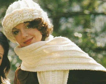 Peut inclure: Une femme portant un chapeau et une écharpe en tricot blanc avec des franges, une veste marron et une bague à son doigt. Elle tient un guidon de vélo.