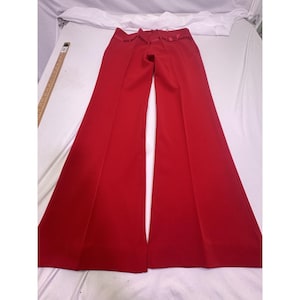 May include: Bright red wide-leg pants. The pants have a high waist and a flared design. The fabric appears to be a smooth, solid color. The pants are laid flat on a white surface, showcasing their full length and shape.