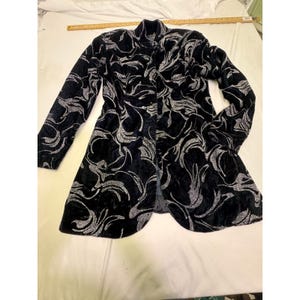 May include: A black velvet coat with a silver floral pattern. The long coat has a notched collar and long sleeves. The coat is open in the front.