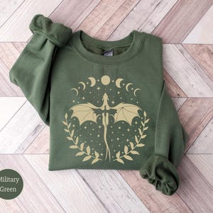 May include: A green sweatshirt with a gold dragon design and a crescent moon and star pattern. The sweatshirt has a crew neck and long sleeves.