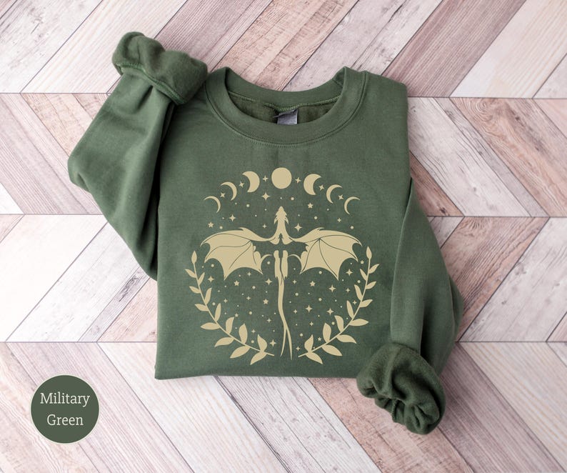 May include: A green sweatshirt with a gold dragon design and a crescent moon and star pattern. The sweatshirt has a crew neck and long sleeves.