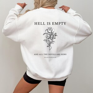 May include: White sweatshirt with the text "HELL IS EMPTY" above a black and white floral and snake design. Below the design, the text reads "AND ALL THE DEVILS ARE HERE" and "WILLIAM SHAKESPEARE". The sweatshirt is a crew neck style.